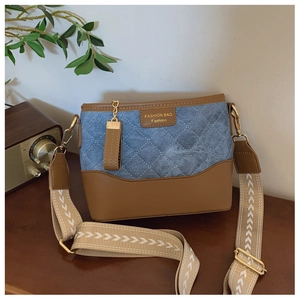 Detail of blue denim and brown leather bucket bag with quilted patterns and wide canvas strap