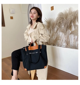 Detail of black canvas tote bag with brown leather handles and white artistic lettering