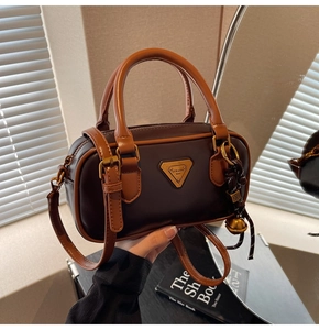 Detail of Boston bag showing textured PU leather, metal logo plaque, and golden bell charm