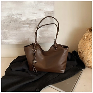 Detail of coffee brown tote bag with unique knot straps and woven pendant on a suit