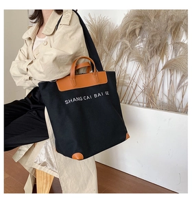 Close-up of black canvas tote bag with brown leather handles and brand lettering detail