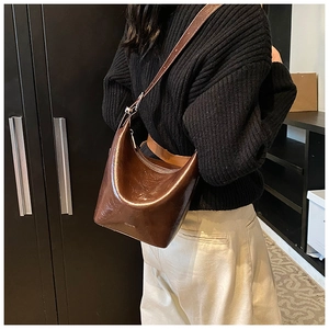 Detail of a shiny brown leather crescent bag with adjustable strap and 'NO FILTER' text