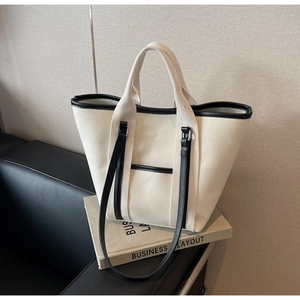 Detail of canvas tote bag with black leather trim and dual straps on a studio setup