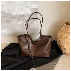 Detail of dark brown leather tote bag with braided charm on a black blazer background