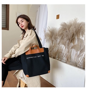 Detail of black canvas tote bag with brown leather handles and side text decoration