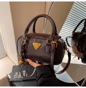 Detail of glossy brown Boston bag with golden triangular logo and charm accessories