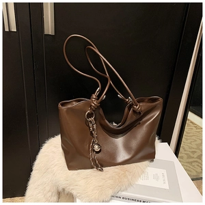 Close-up of brown leather tote bag showing knot strap and metal sphere pendant detail