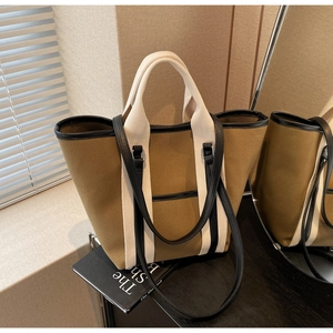 Detail of khaki canvas tote bag with contrast cream handles and black leather trim