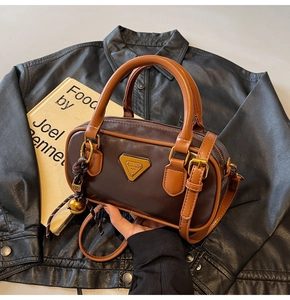 Detail of a vintage dark brown Boston bag with caramel handles and metal logo plate