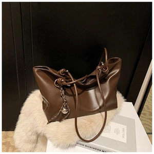 Close-up of a brown leather tote bag with knot detail and golden bell charm on soft faux fur