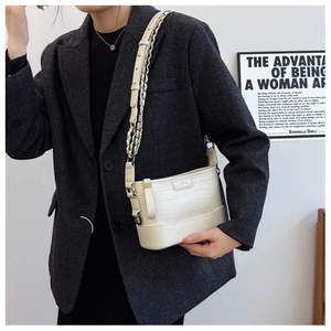 Detail of white crocodile embossed bucket bag with metal chain strap on grey blazer