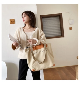 Detail of canvas tote bag with brown leather trim and printed letter design on front