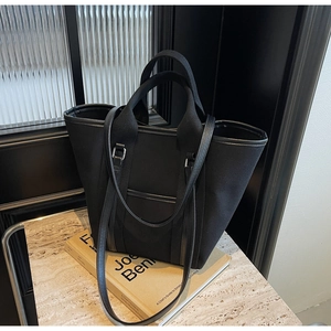 Detail of a black canvas tote bag with leather trim on a marble surface and books