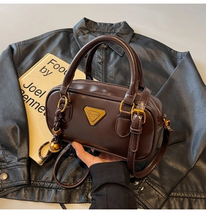 Close-up of a dark brown matte leather pillow bag featuring a gold triangular logo plate