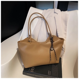 Detail of khaki leather tote bag featuring a scalloped edge and braided rope pendant