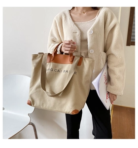 Close-up of beige canvas tote with brown leather trim and stylish letter printing