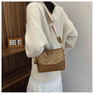 Close-up of brown quilted crossbody bucket bag with wide strap on a model outfit