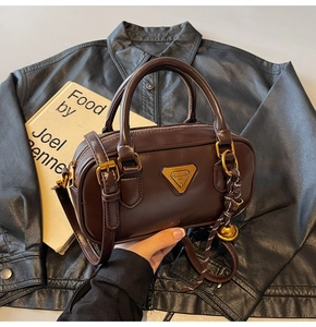 Detail of dark brown leather Boston bag with metal logo and bell charm accessory