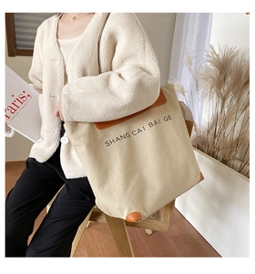 Detail of canvas tote bag featuring brown leather trim and printed letters in a lifestyle setting