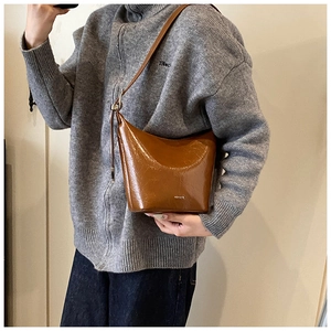 Close-up of caramel brown glossy leather bag with metal buckle and shoulder strap detail