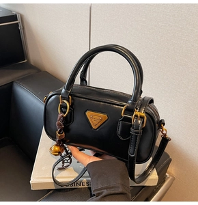 Detail of black Boston bag featuring gold triangle logo and ornate bell bag charm