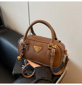 Detailed close-up of a brown leather Boston bag with metal logo and woven bell charm