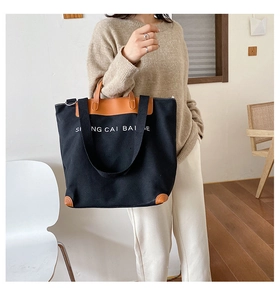 Detail of canvas tote bag showing contrast leather trim and printed letter branding