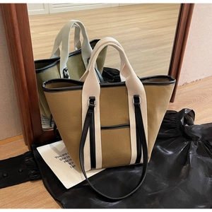 Detail of khaki canvas tote bag with black piping and woven handles in mirror reflection