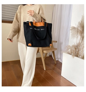 Detail of high-density black canvas tote with brown leather corners and branded print
