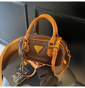 Detail of a brown leather Boston bag with a gold logo and woven pendant decoration