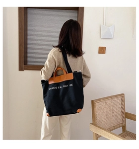 Rear view of large black canvas tote bag with brown leather details on model shoulder