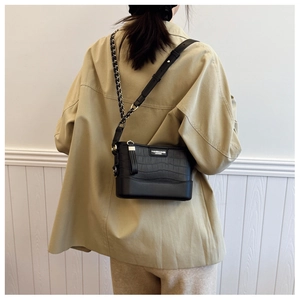 Detail of black crocodile texture bucket bag with metal chain strap worn by a model