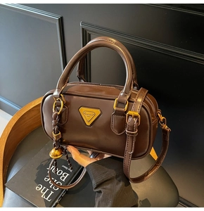 Detail of dark brown leather pillow bag with gold triangle plate and dual handles