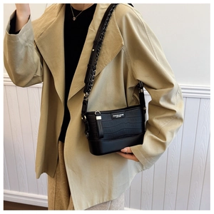 Detail of black crocodile pattern crossbody bag styled with a beige trench coat