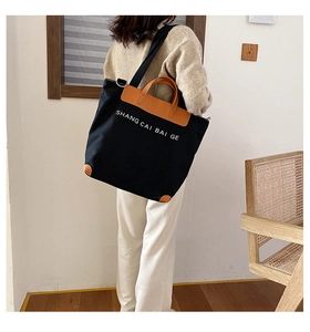 Detailed view of the large canvas tote bag with brown leather trim on a model shoulder