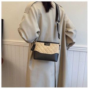 Close-up of quilted beige and black crossbody bag with geometric woven strap on model