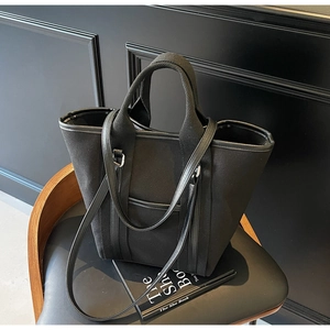 Detail of black canvas tote bag with leather trim and shoulder strap on a chair