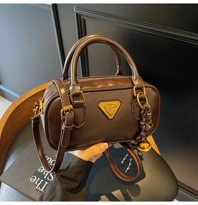 Detail of a dark brown mini Boston bag with gold logo plaque and leather texture