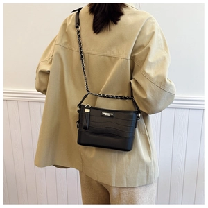 Detail of black crocodile texture bag with gold chain strap on khaky jacket