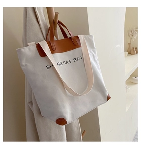 Detail of large canvas tote bag with brown leather accents hanging on wooden rack