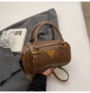 Detail of a brown leather boston bag with a triangular golden metal logo plaque