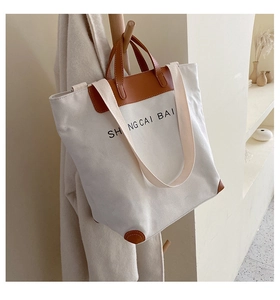 Detail of off-white canvas tote with brown leather handles and reinforced corner guards