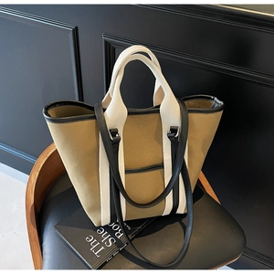 Detail of olive canvas tote bag with white webbing handles on a black leather chair