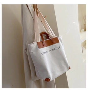Detail of canvas tote bag with brown leather accents and brand lettering on front