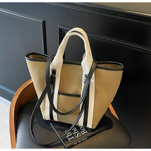 Close-up of canvas tote bag with thick cream handles and black leather trim detail