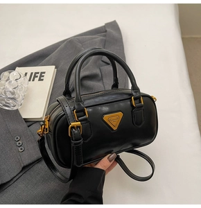 Detail of black matte Boston bag with gold triangular metal logo and adjustable strap
