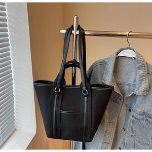 Close-up of black canvas tote bag with dual handles and front leather-trimmed pocket