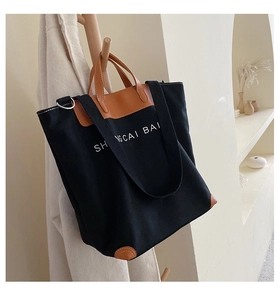 Detail of black canvas tote bag featuring brown leather trim and white typography on strap