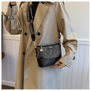 Detail of grey quilted shoulder bag with herringbone strap worn with a beige trench coat