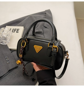 Close-up of black leather Boston bag with gold triangle logo and bell charm accessory